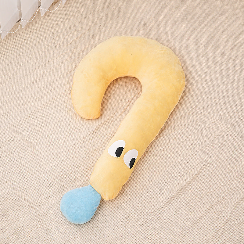 Yellow U-shaped pillow with a blue tip and cartoon face on a beige surface