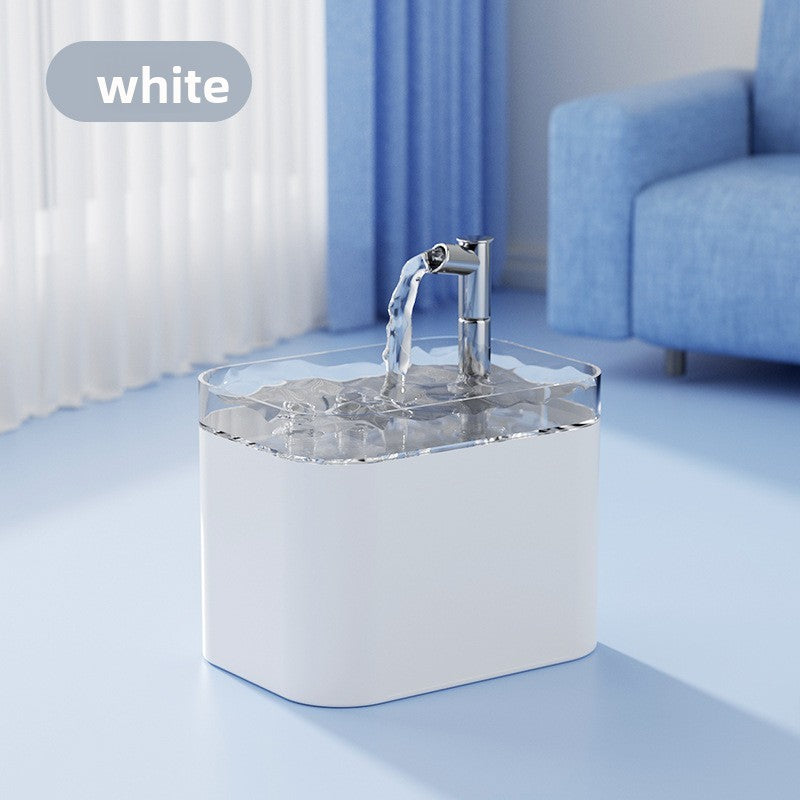 A white rectangular water dispenser with a clear lid and a chrome faucet spout, shown with water flowing from the spout. The product is set in a bright, modern room with a blue sofa and curtains in the background.
