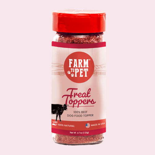 A bottle of Farm to Pet Treat Toppers, 100% Beef Dog Food Topper, featuring a red cap and a cream label with a red circular logo, set against a solid pale pink background.