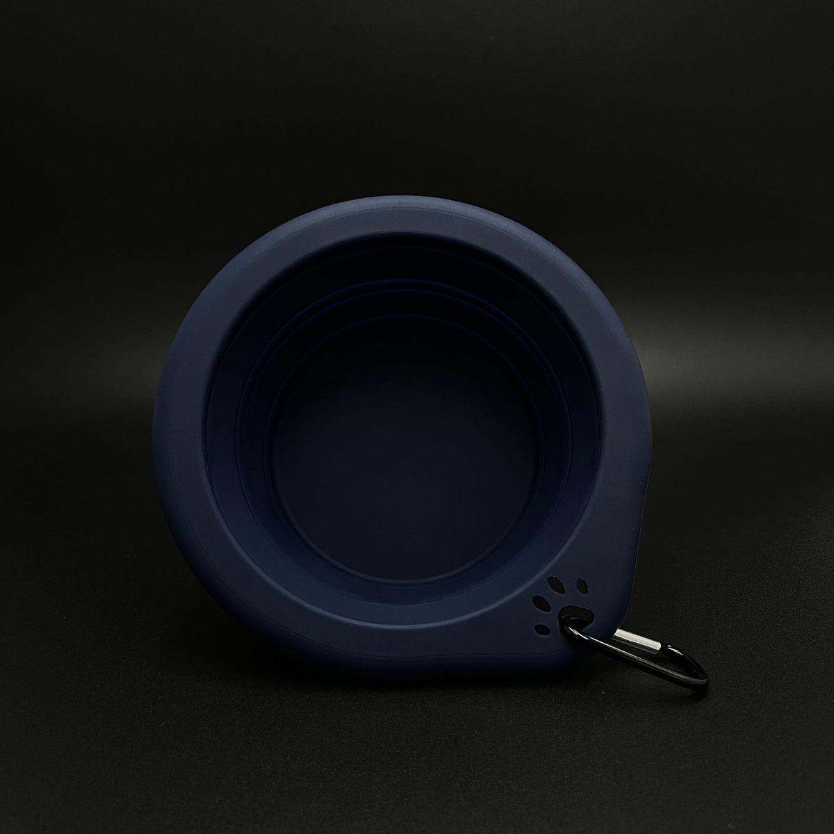 A dark navy blue collapsible silicone bowl with a black metal carabiner clip, shown on a dark background.