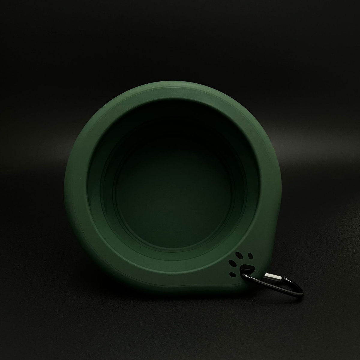 A dark green collapsible silicone pet bowl with a black metal keyring attached, shown against a dark black background.
