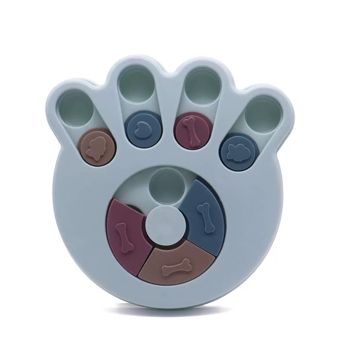A silicone dog toy shaped like a paw print, featuring a light blue base with five raised pads and a circular wheel section in the center. The toy includes small, colorful, bone-shaped compartments in brown, blue, and pink, all on a clean white background.